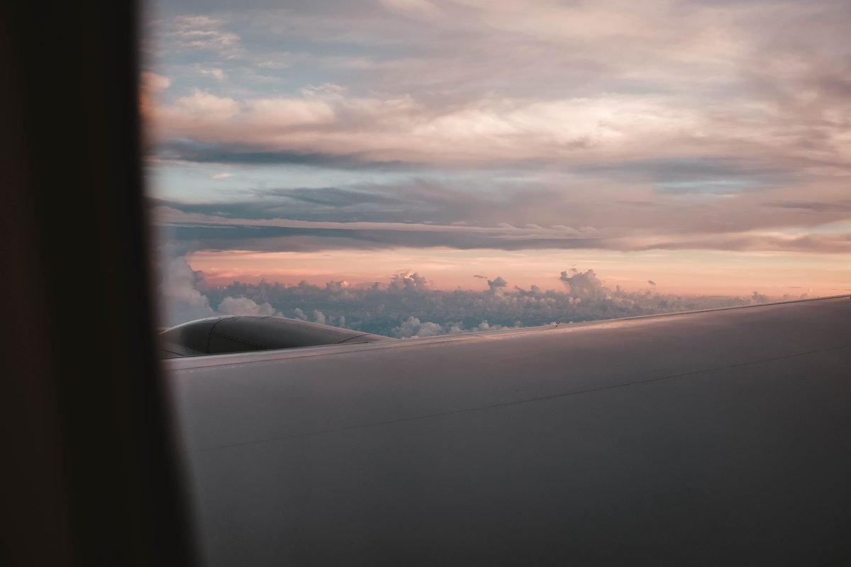 View from an airplane window showing the wing and sunset skies above clouds.