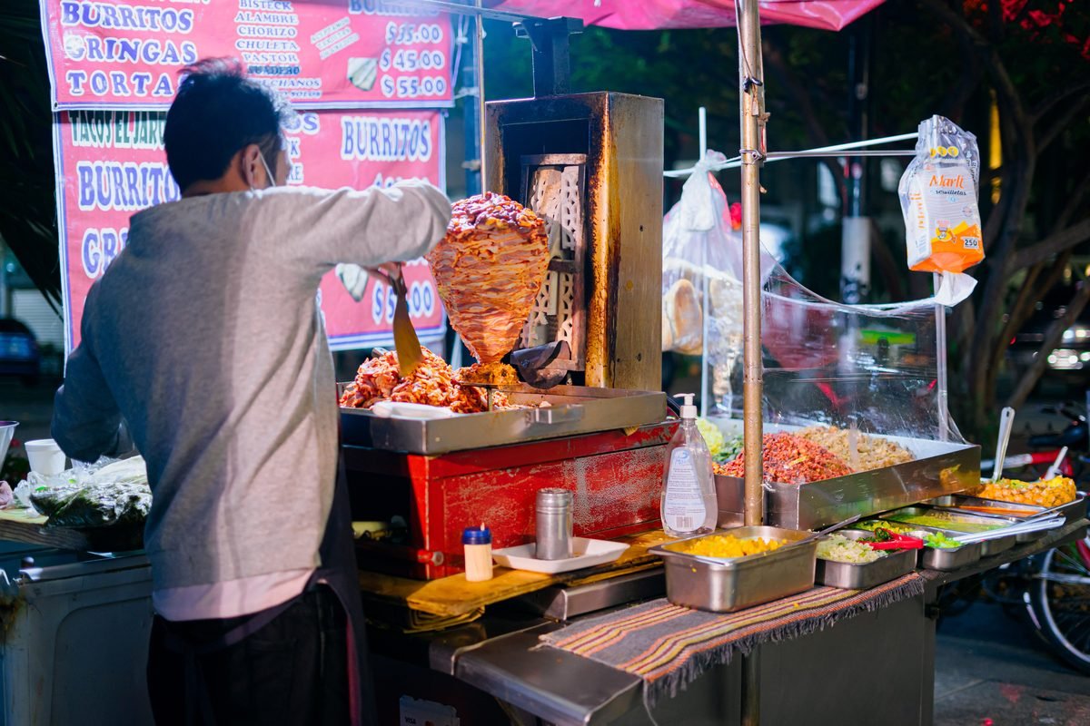 Street vendor cooking tacos al pastor at a night market stand