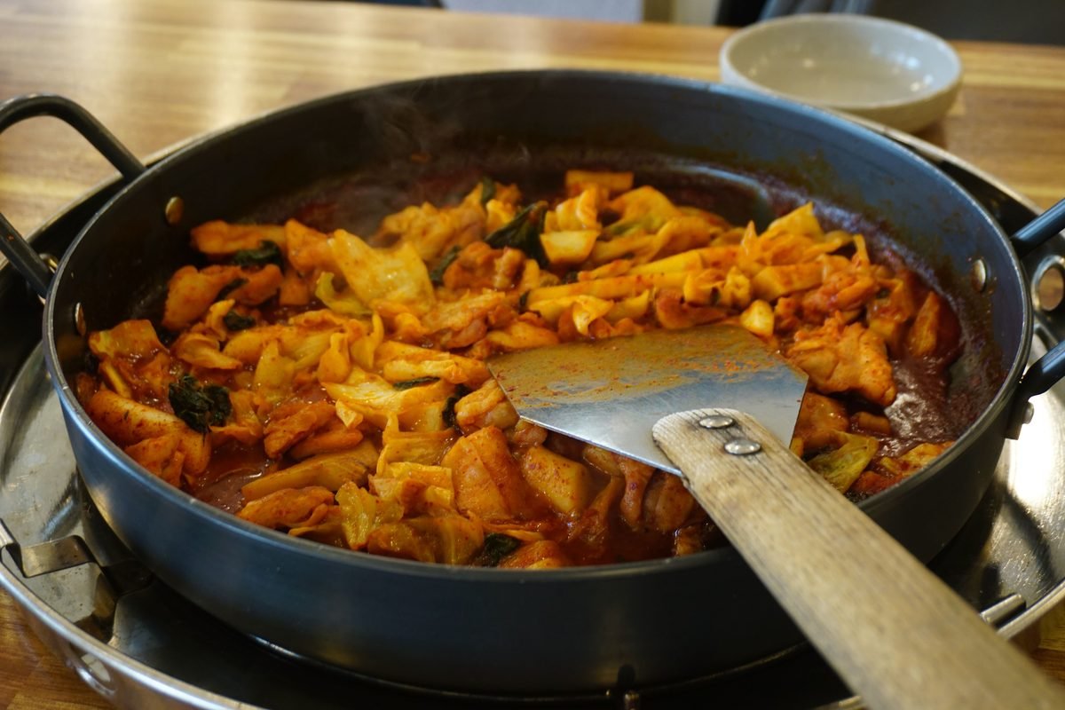 Spicy red dakgalbi cooking in a large round iron pan with a spatula
