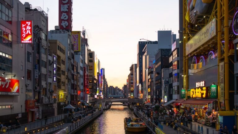 Dotonbori canal at sunset with colorful neon signs and pedestrian walkways in Osaka