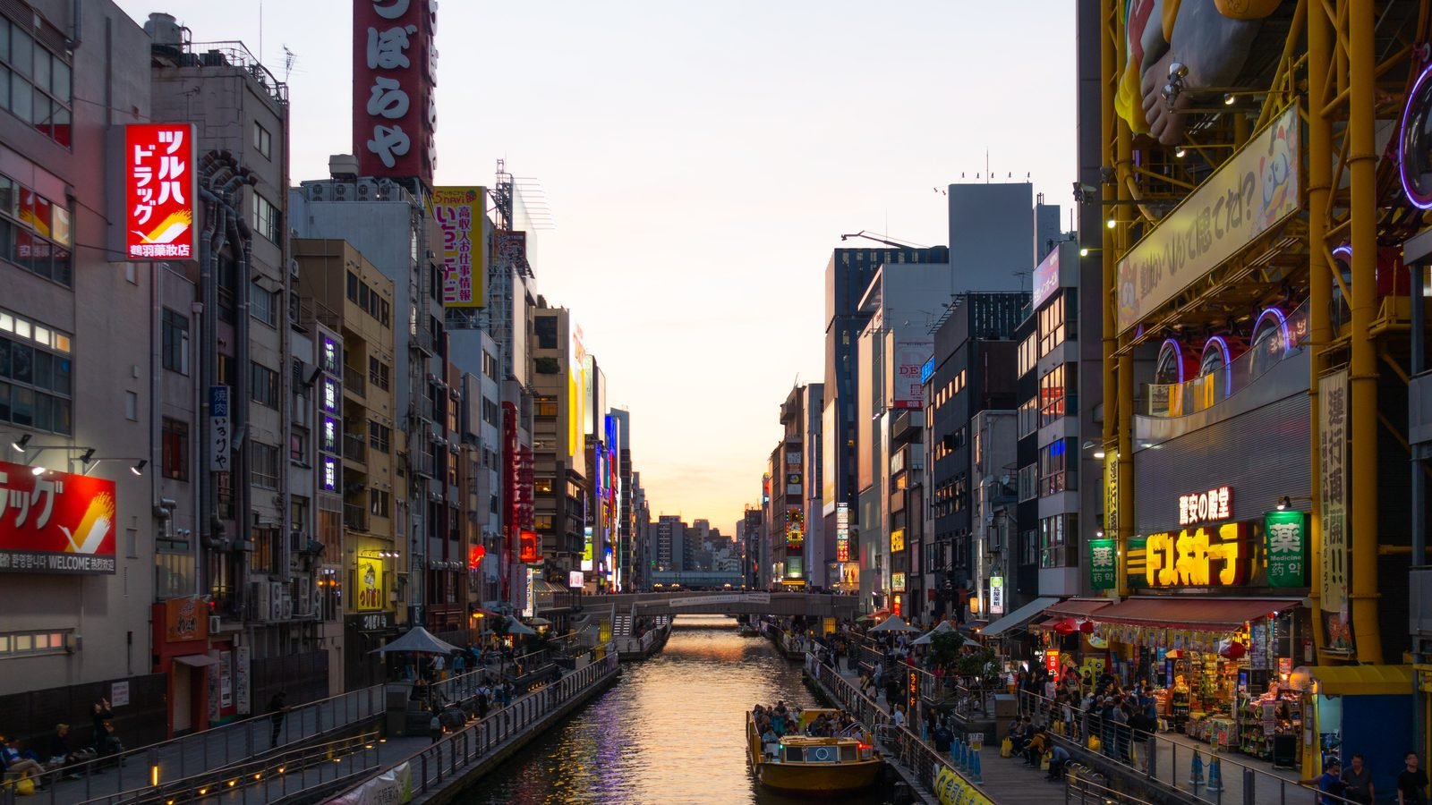 Dotonbori canal at sunset with colorful neon signs and pedestrian walkways in Osaka