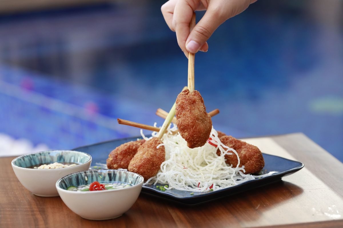 Hand holding deep-fried skewers with dipping sauces on a table