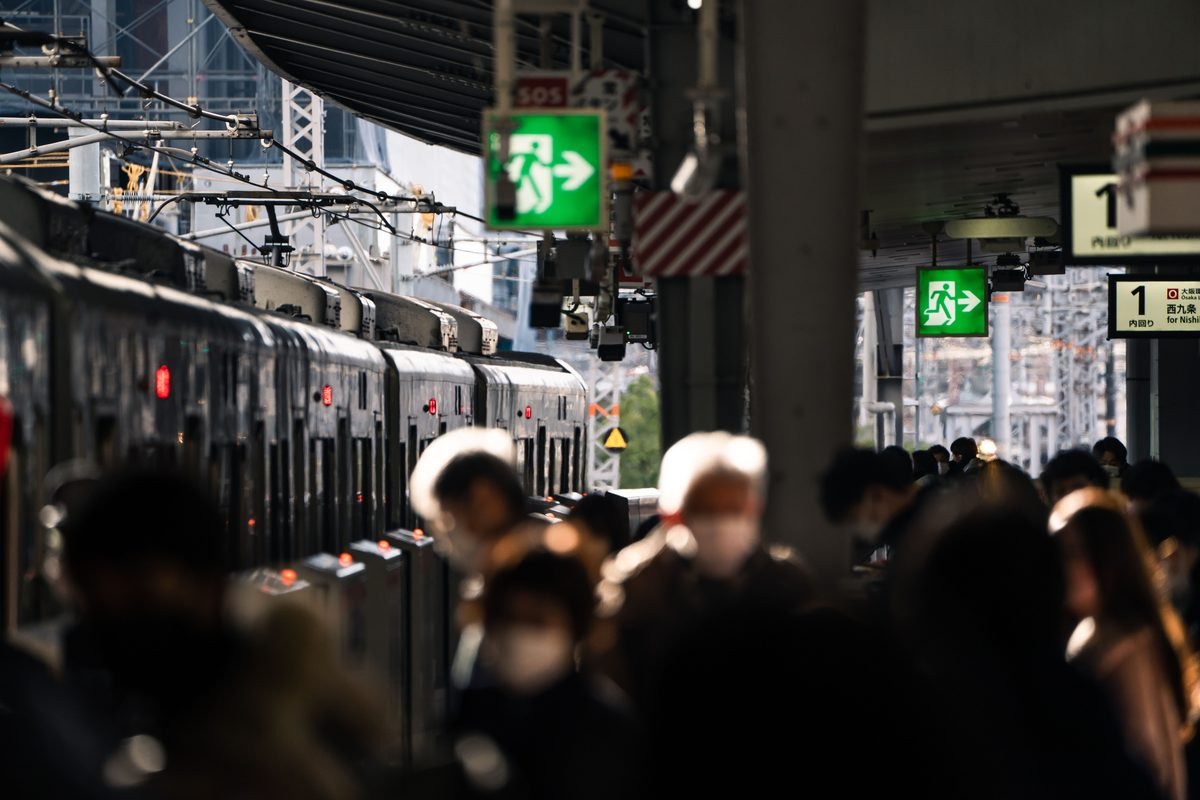 Crowded train station platform in Japan with commuters waiting by tracks.