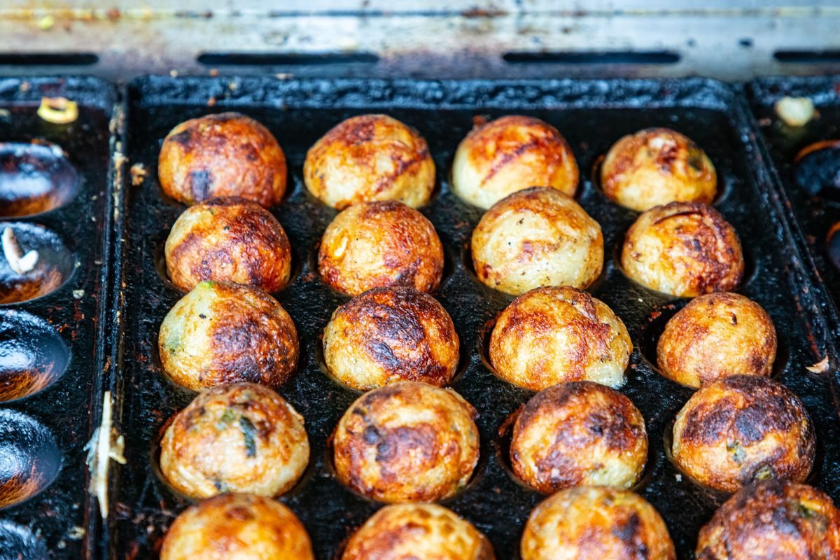 Golden brown takoyaki balls cooking on a traditional cast iron grill