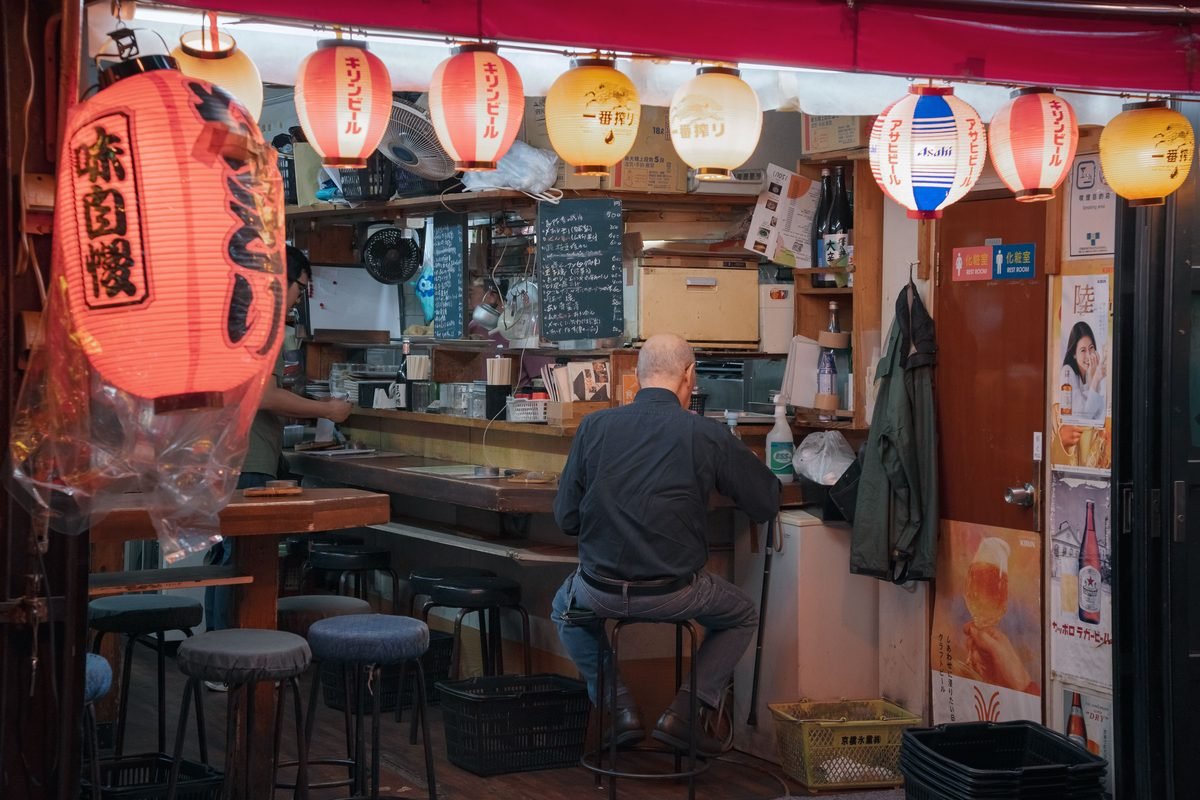 Customer sitting at a counter inside a cozy Japanese izakaya bar with red lanterns