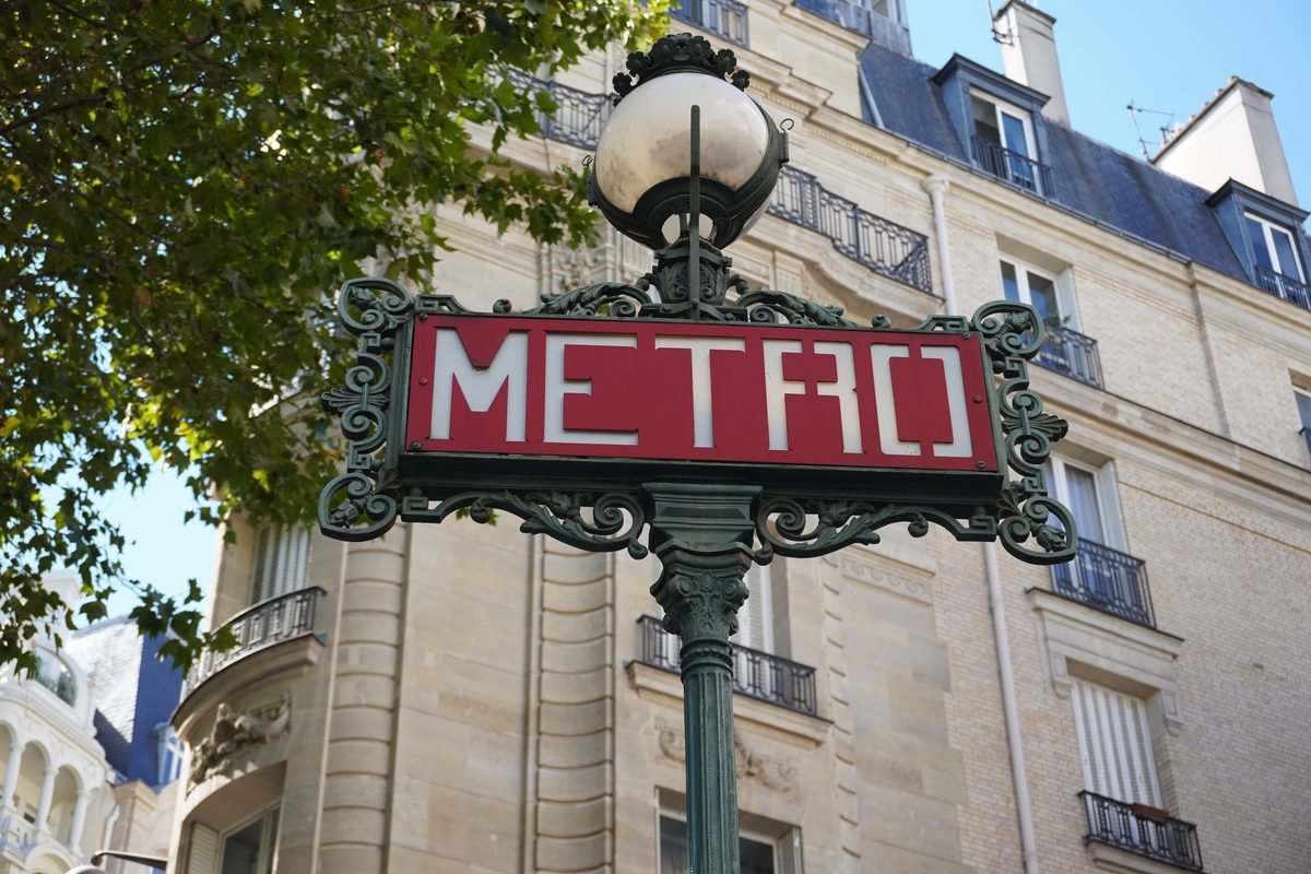 Red Metro sign with ornate green ironwork against Parisian architecture