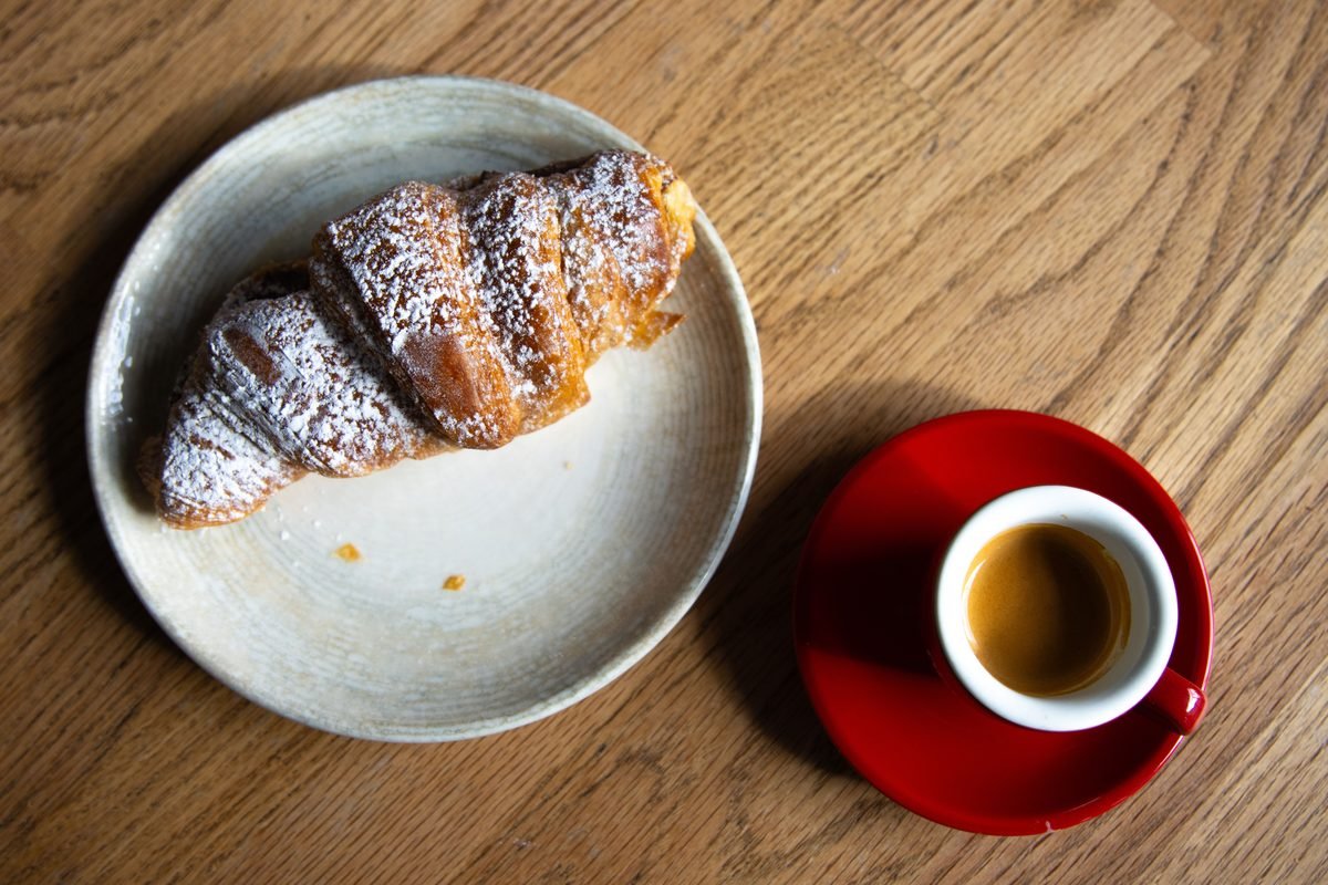 Flaky croissant on a plate with a cup of espresso on wooden table
