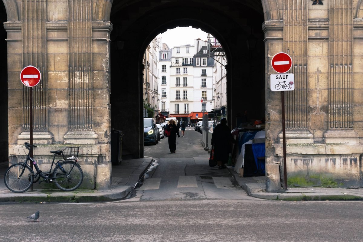 Historical archway framing a Parisian street scene with bicycles and pedestrians