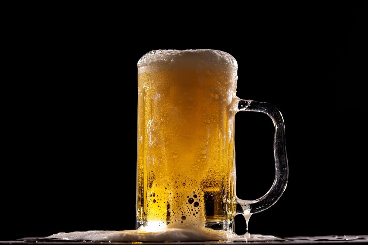 Fresh mug of golden beer with thick white foam against a dark background