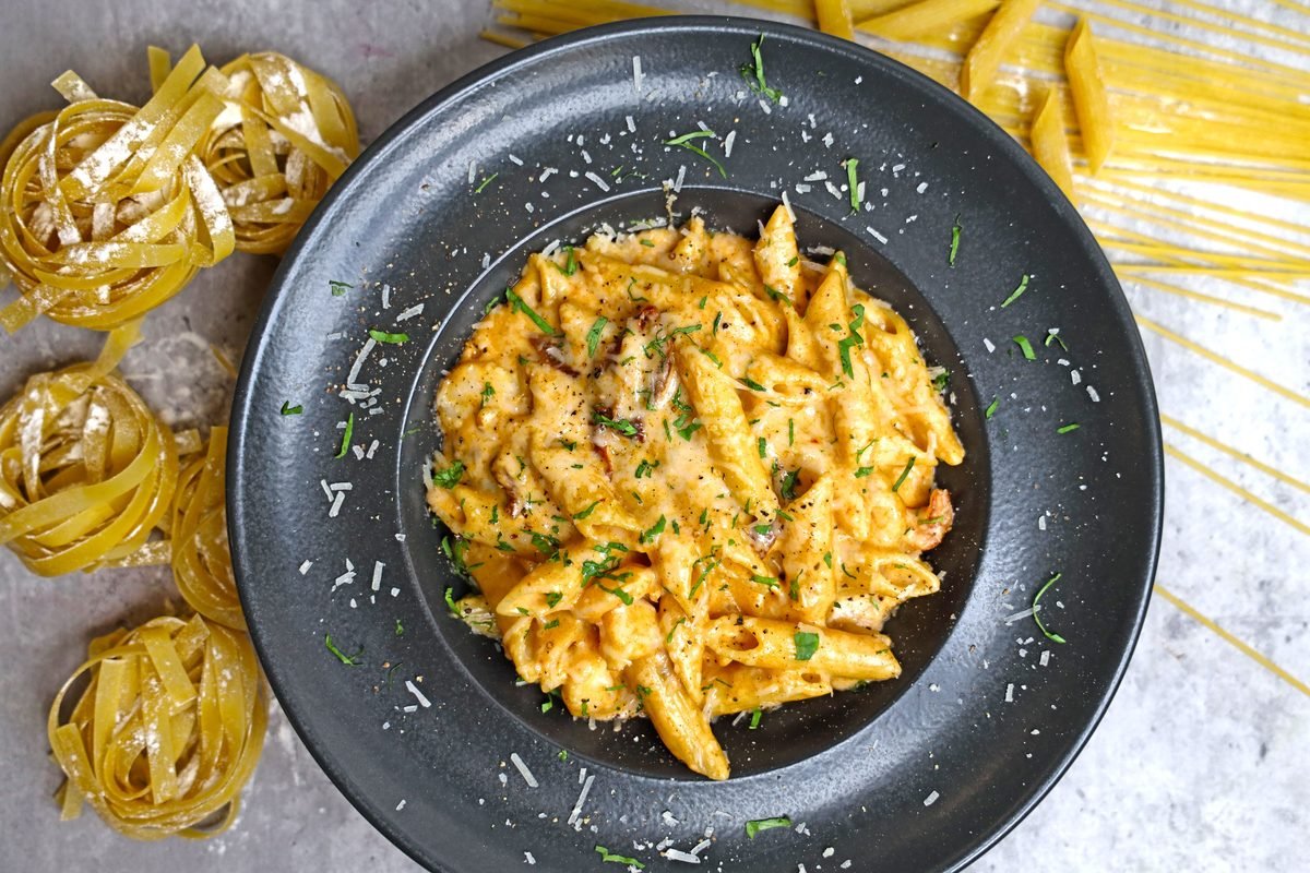 Creamy pasta dish served on a dark plate with herbs and cheese.