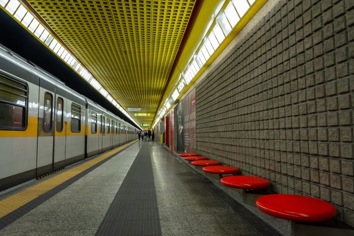 A modern subway station platform with yellow ceiling and red seating