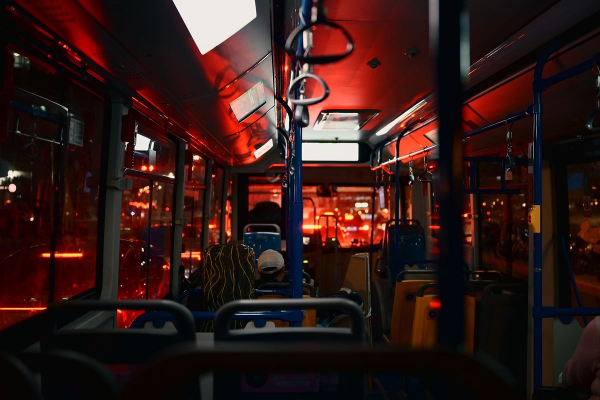 Nighttime interior of a city bus with passengers under red lighting.