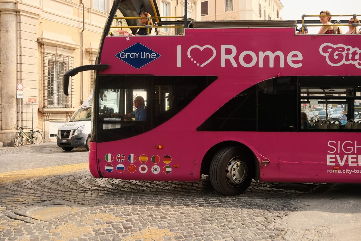 Vibrant pink tour bus operating on a cobbled street in Rome.