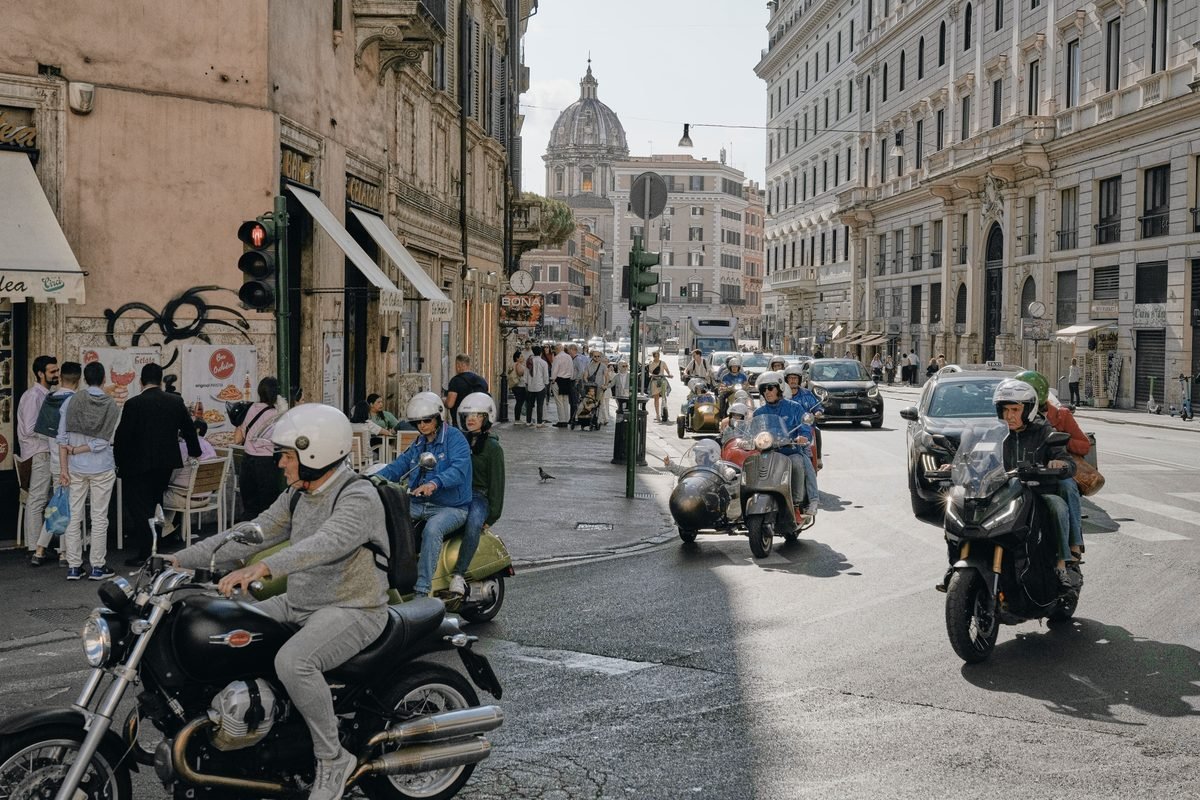 Scooters and pedestrians navigating a bustling street in Rome.