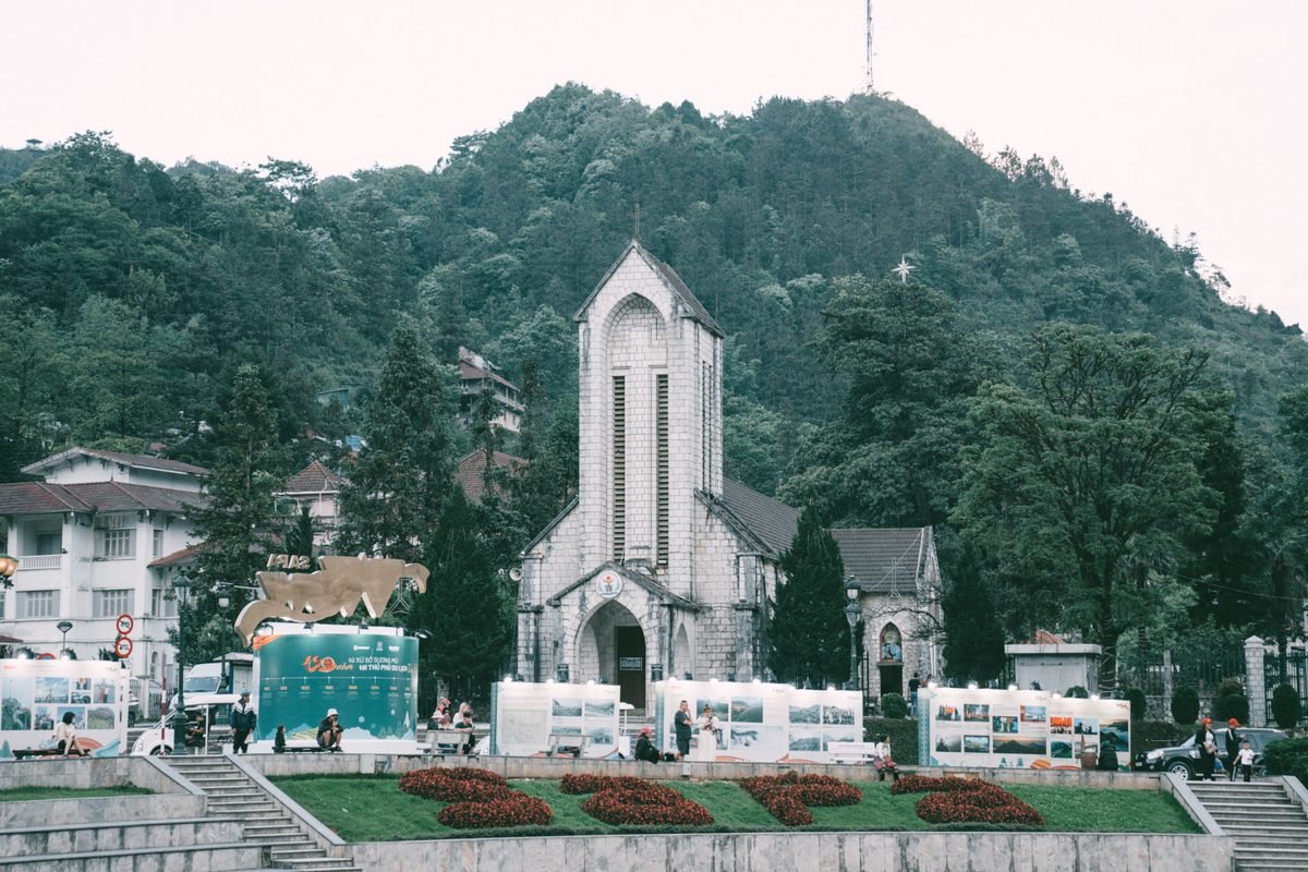 Stone church facade surrounded by greenery and cityscape in Sapa.