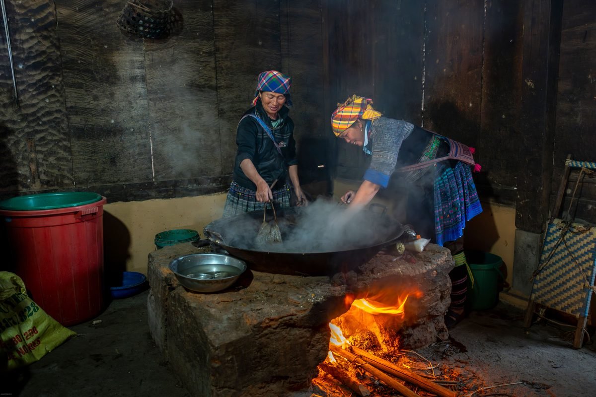 Hmong women cooking over an open fire inside a traditional wooden home in Sapa.