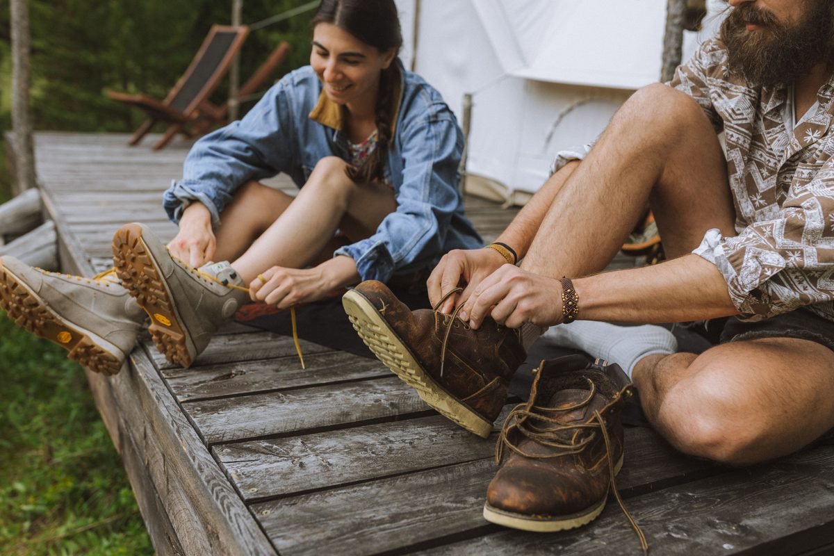 A couple tying their hiking boots on a wooden deck outdoors.