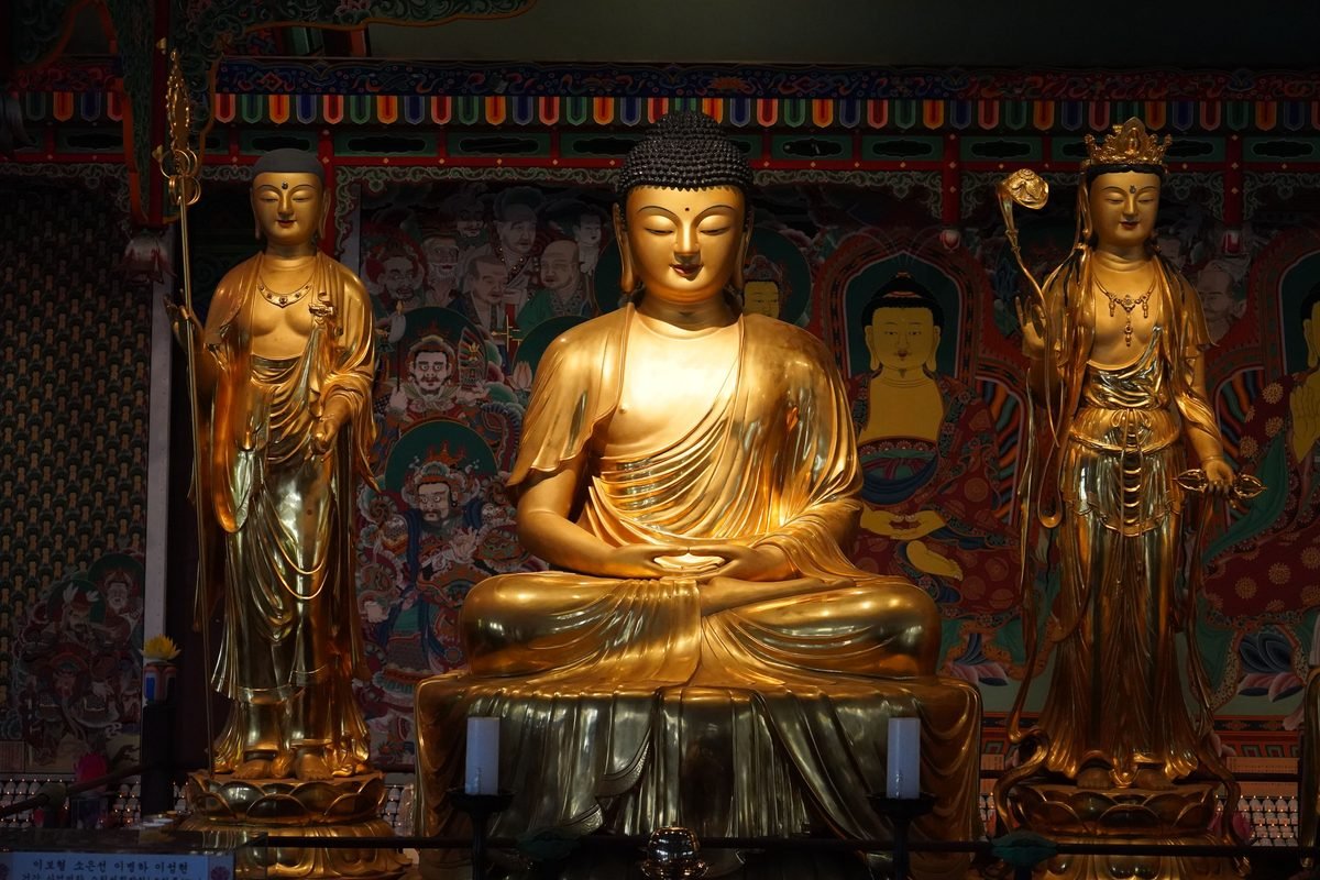 Golden Buddhist statues inside an ornate temple setting.