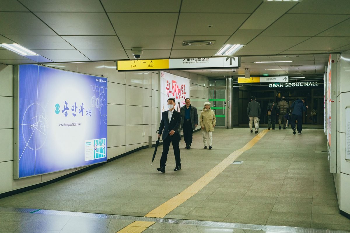 Commuters walking in a Seoul subway station under directional signs.