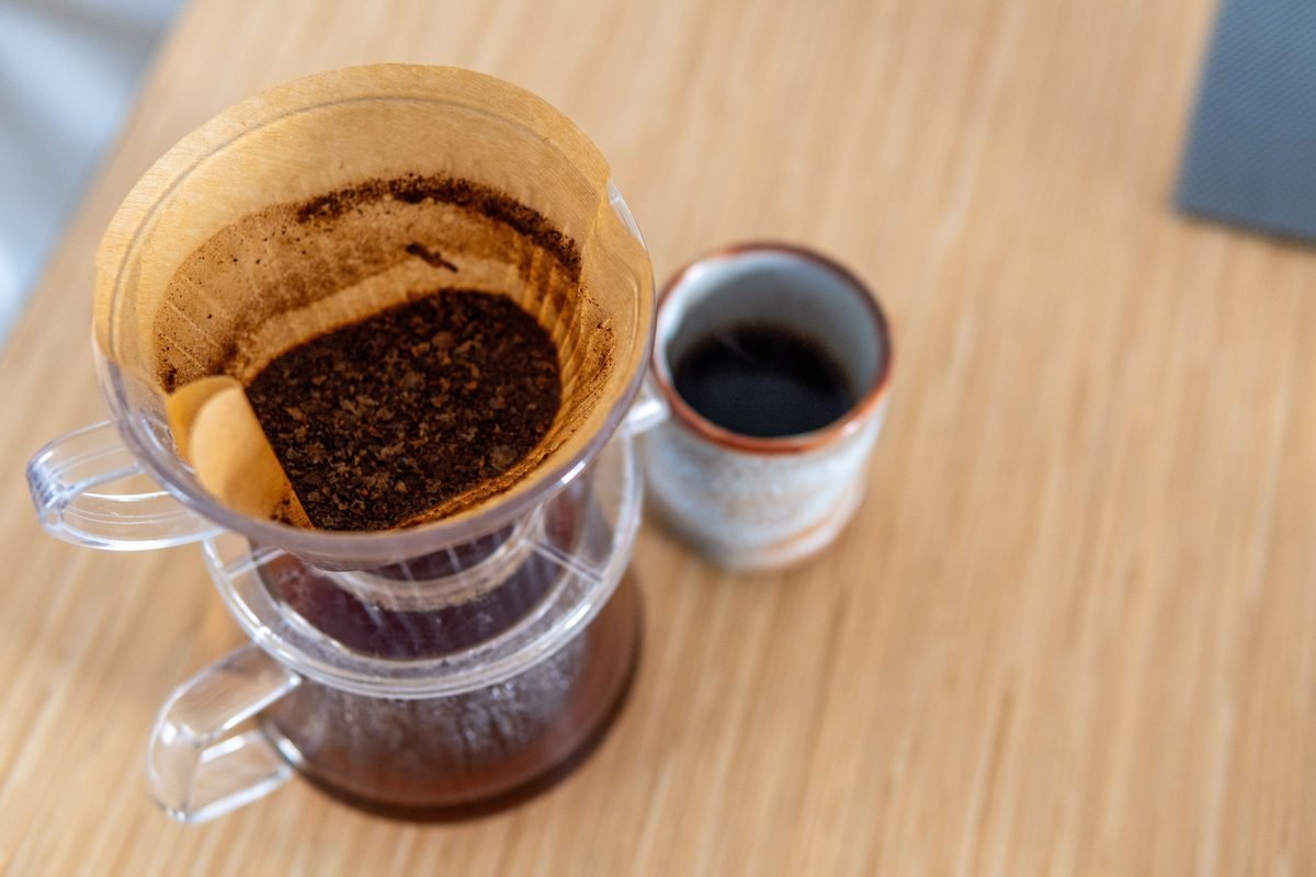 Top-down view of pour-over coffee in a filter next to a ceramic mug.