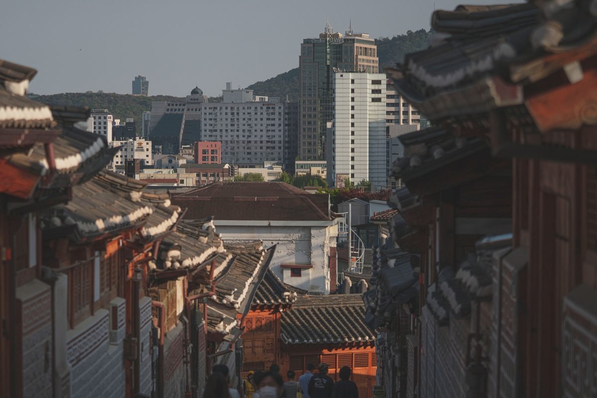 Narrow alley lined with traditional Korean architecture and a modern city skyline.