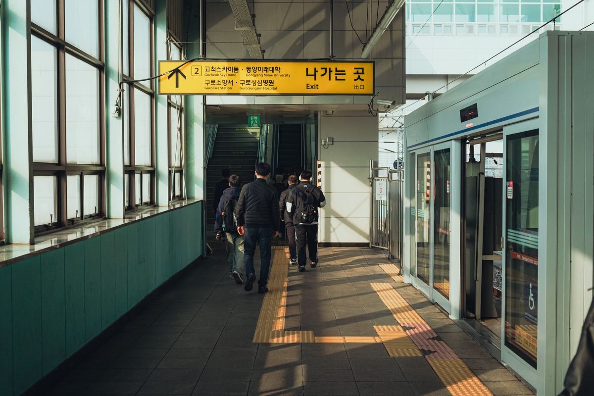 Commuters walking towards an exit with Korean signage at a Seoul subway station.