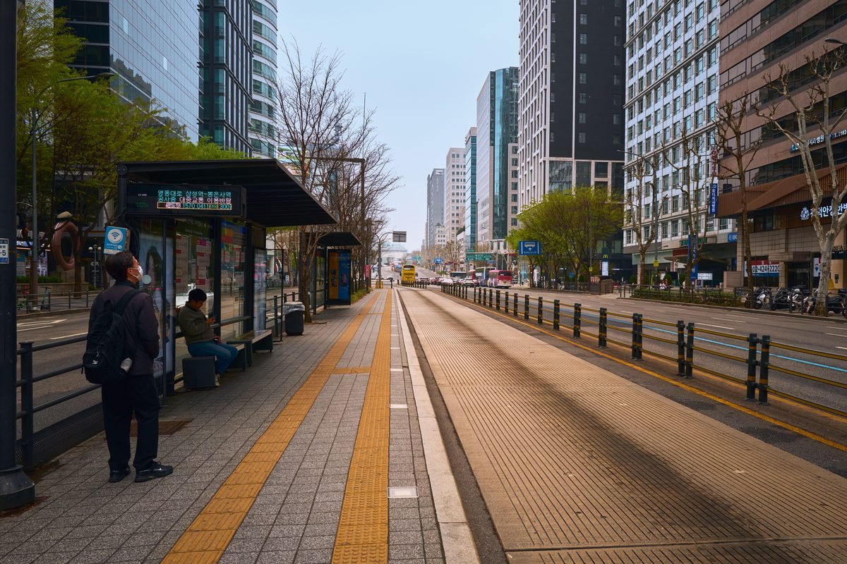 Wide city street flanked by skyscrapers and bus stops in Seoul.