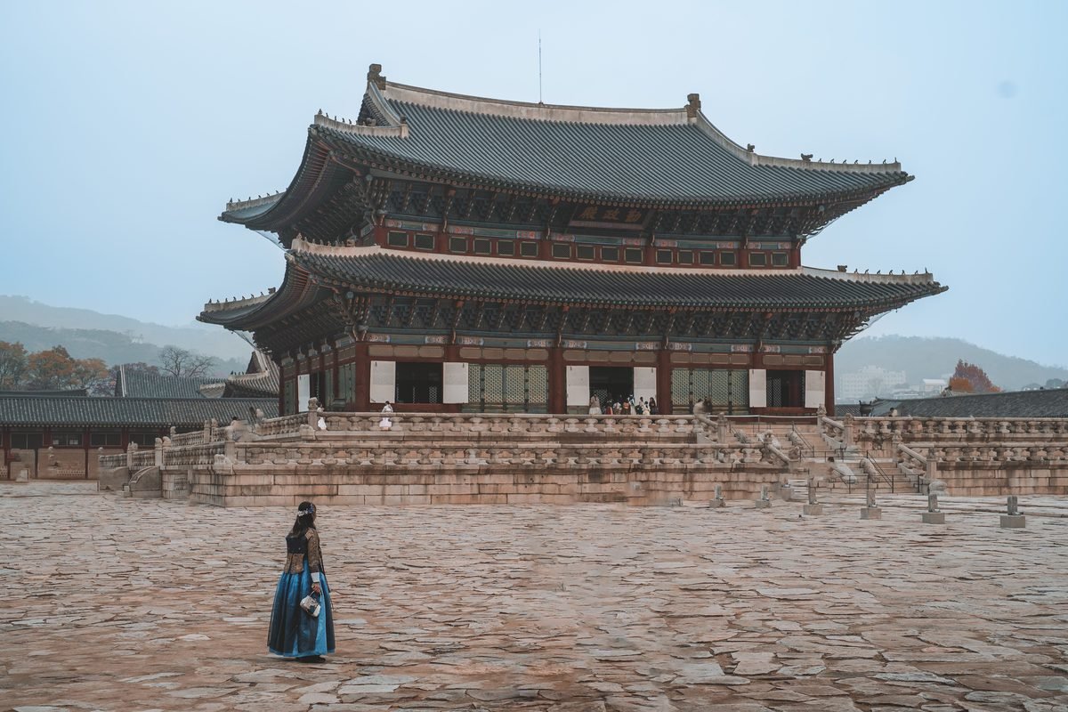Woman in traditional hanbok attire walking past Gyeongbokgung Palace in Seoul.
