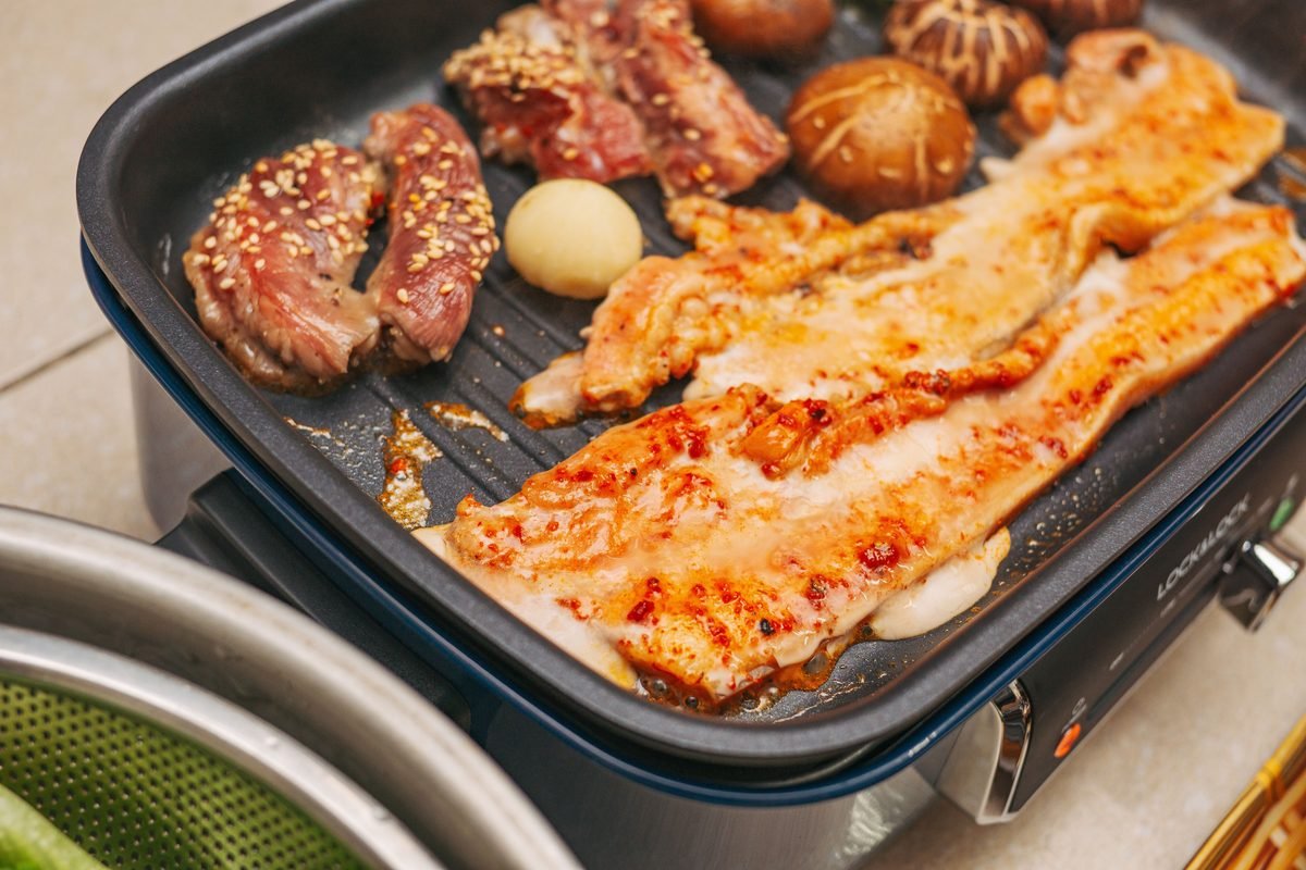 Korean BBQ with pork belly, beef, mushrooms, and garlic sizzling on a grill.