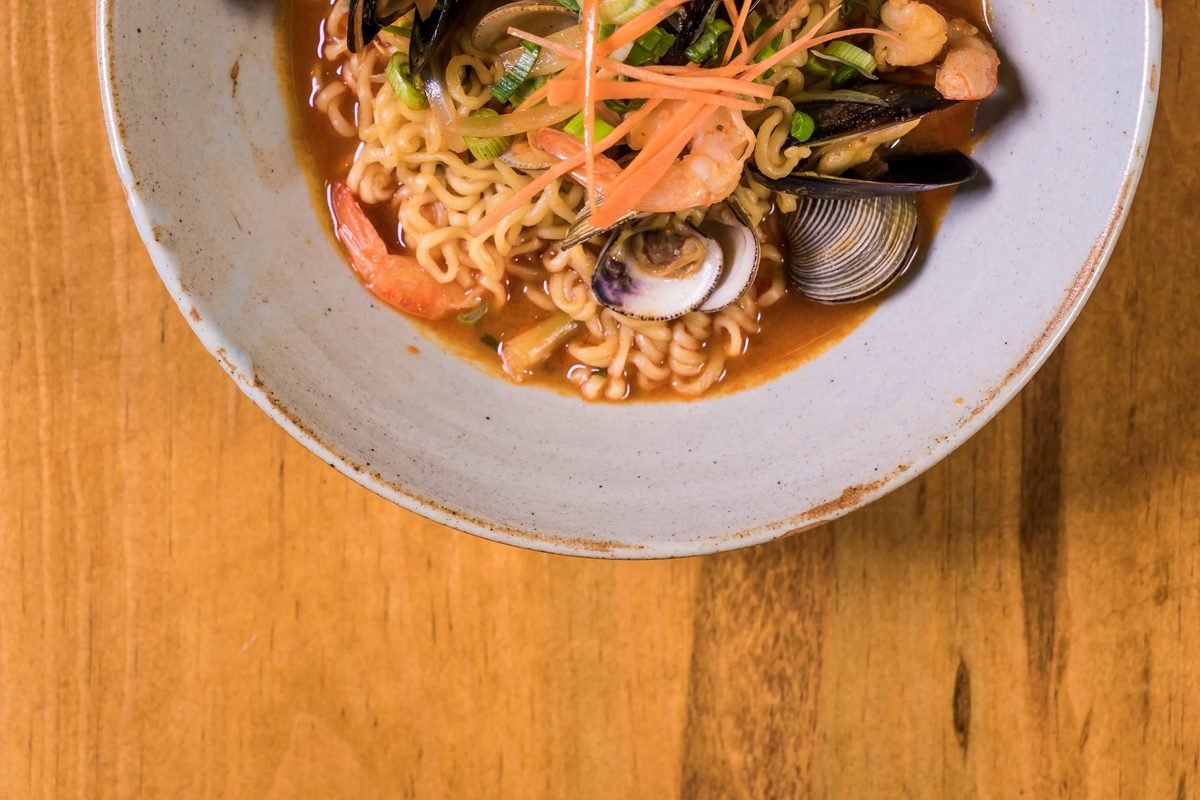 Bowl of seafood ramen with shrimp and mussels on a wooden table.
