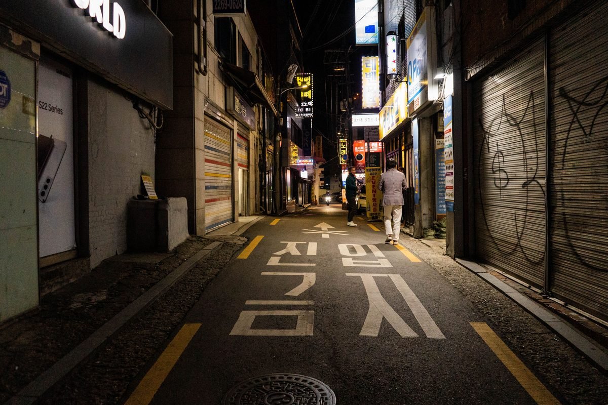 Narrow night street in Seoul with lit storefronts and signage