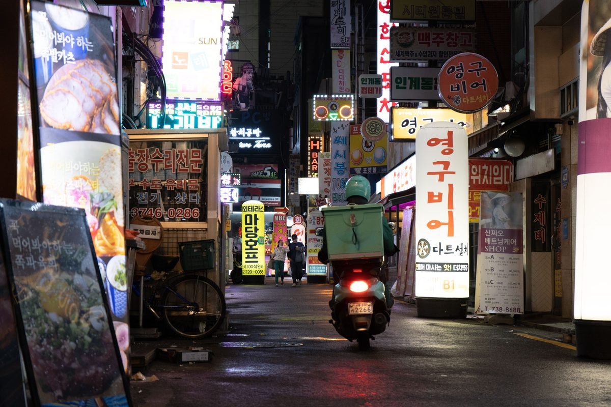 Bustling city street at night with neon signs and a delivery scooter.