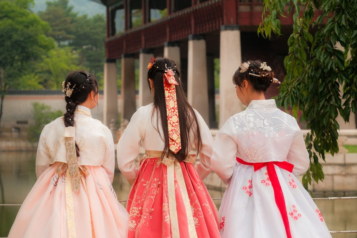 Three female friends wearing colorful hanbok explore a traditional setting in Seoul.
