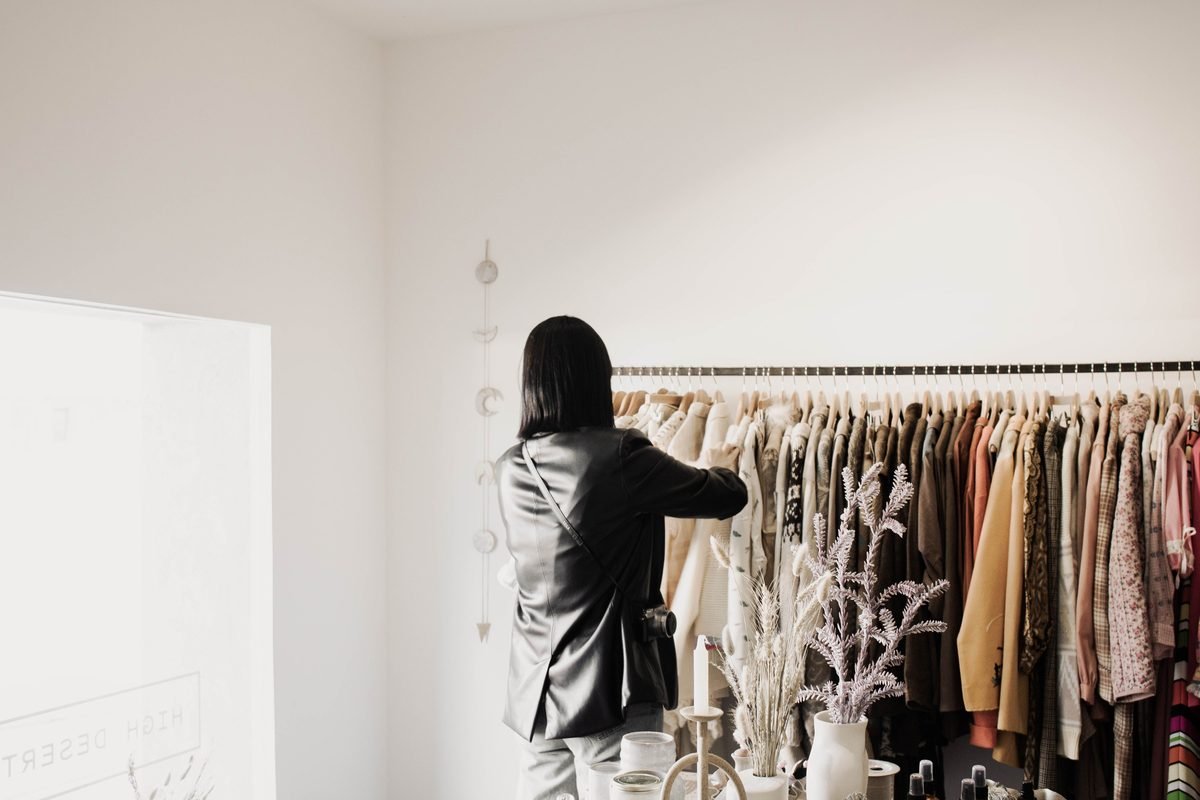 A woman browsing jackets in a bright minimalist clothing boutique.