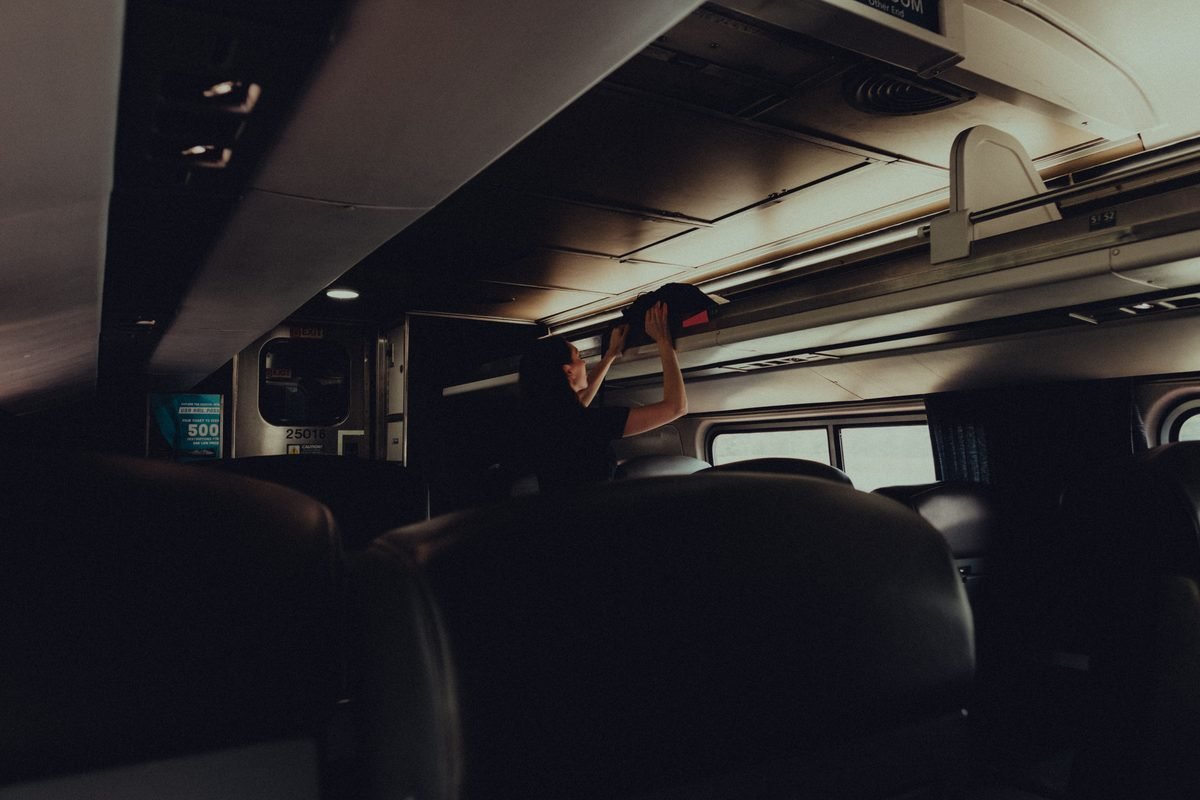 Passenger stowing luggage in overhead train rack.