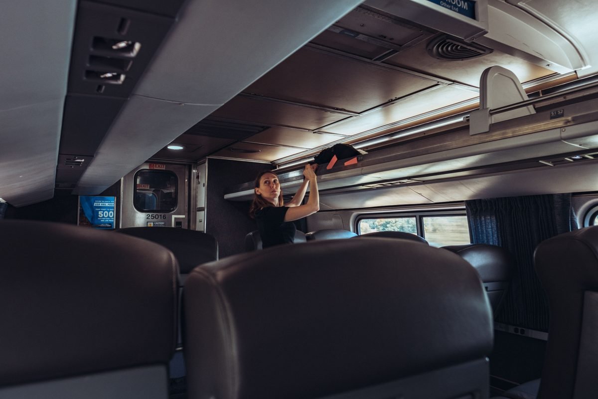 Female traveler stowing luggage in overhead train compartment.