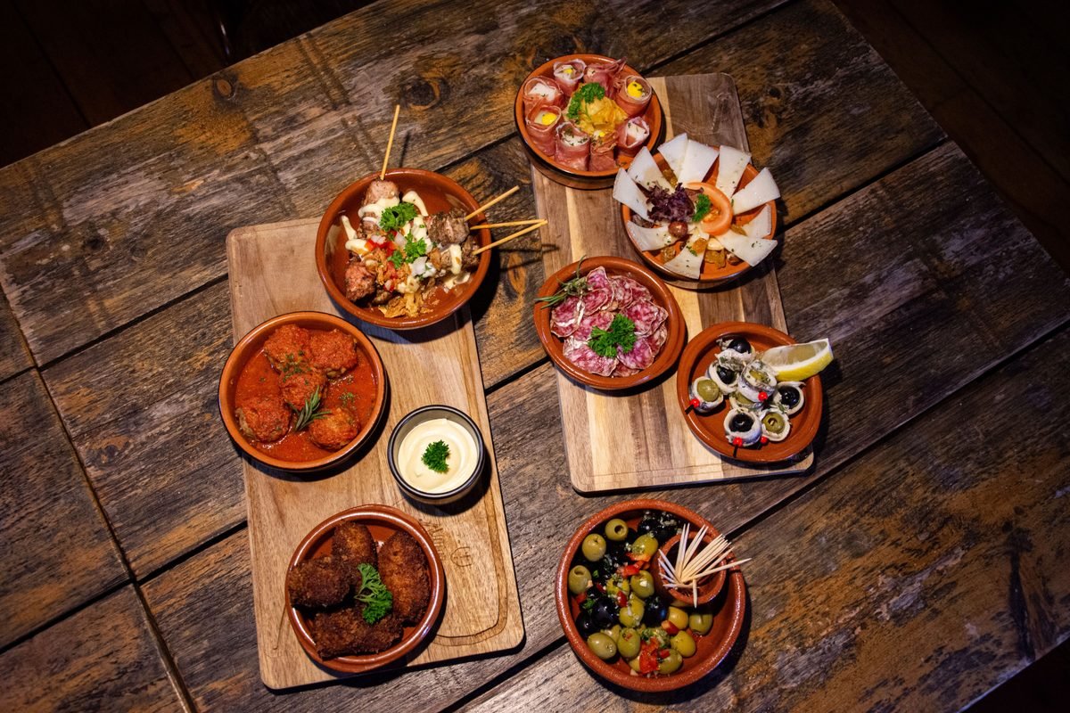 Variety of Spanish tapas dishes served in small clay bowls on a rustic wooden table.