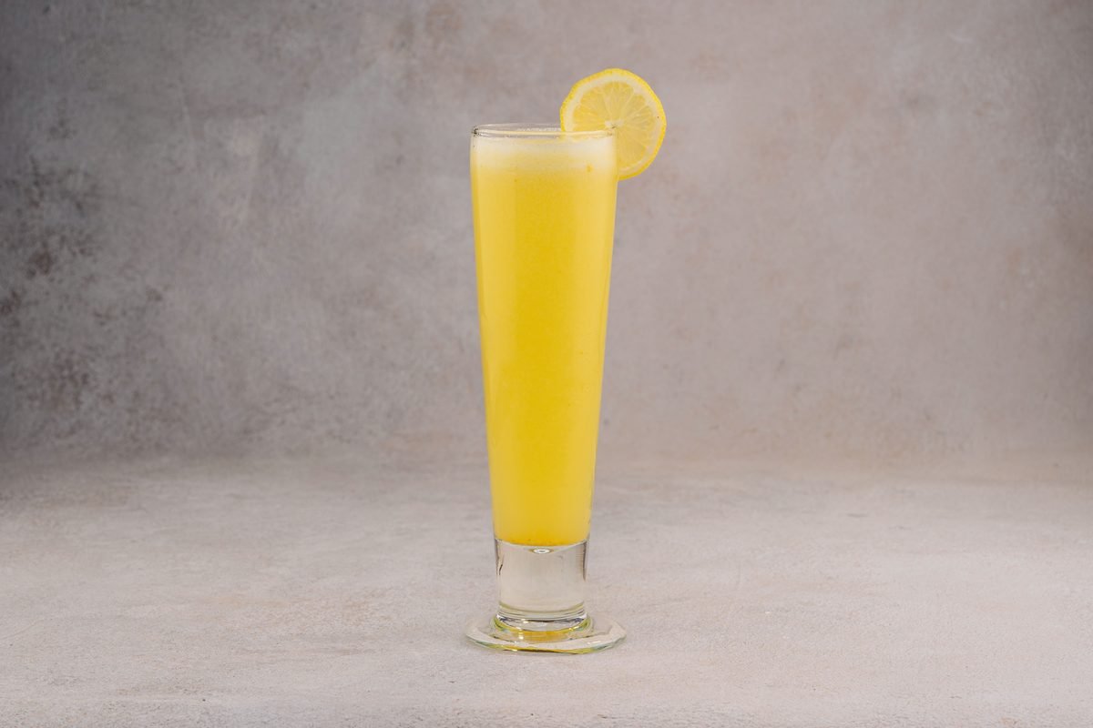 Tall glass of fresh yellow juice with a lemon slice garnish