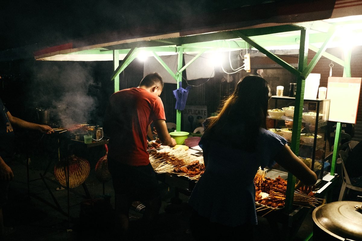 Night scene of street food vendors grilling meat skewers under lights