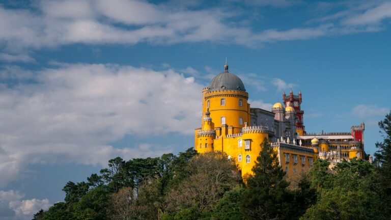 Colorful yellow Pena Palace towers rising above lush green forest against a blue sky in Sintra