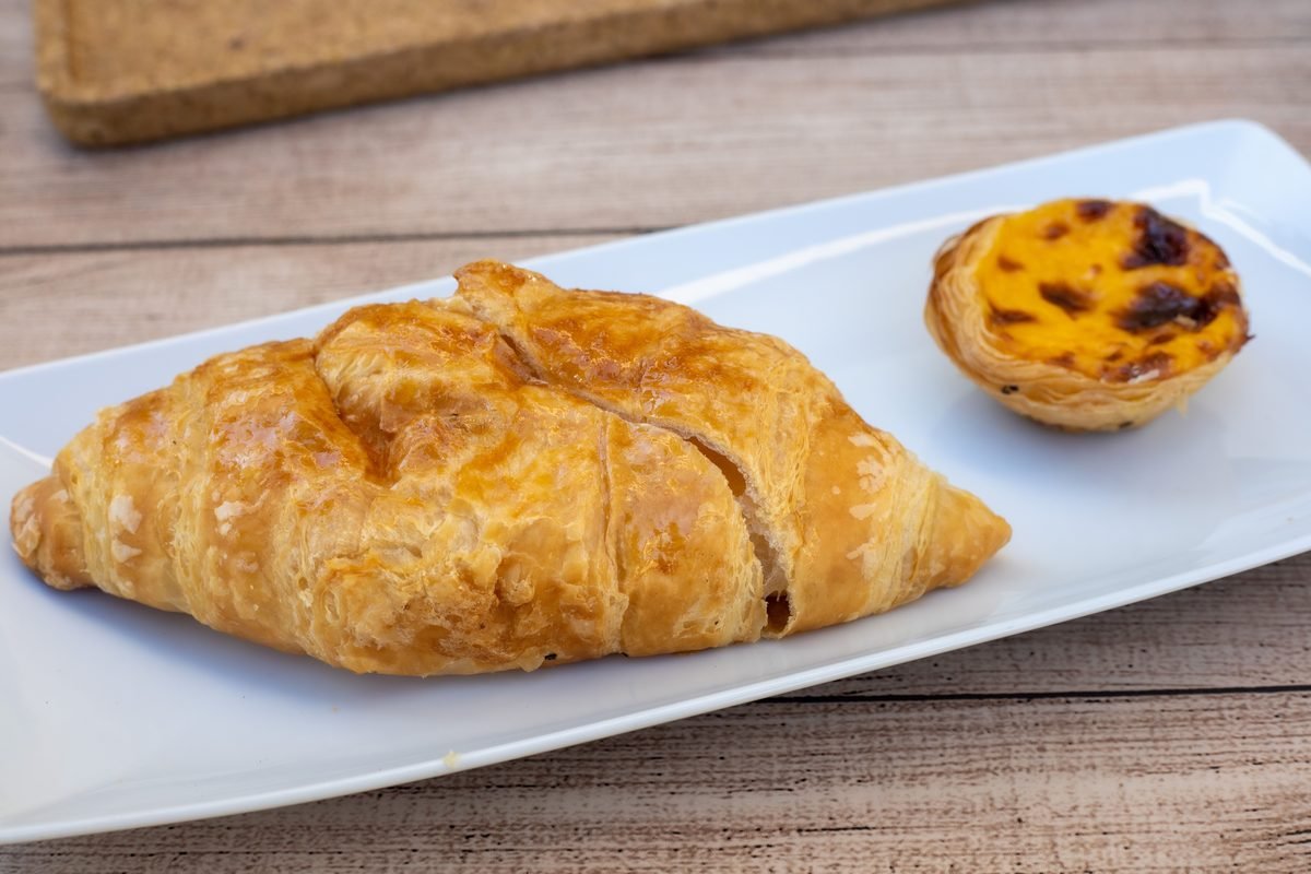 Fresh golden croissant and pastel de nata on a white plate