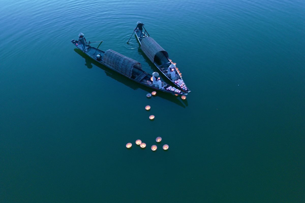 Traditional wooden boats with lit lanterns floating on calm river water at dusk.