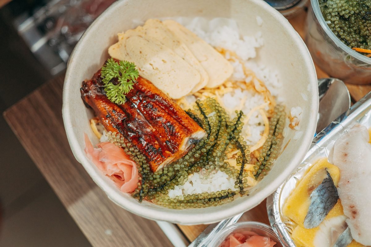 Bowl of Japanese unagi rice with seaweed, tamagoyaki, and pickled ginger.