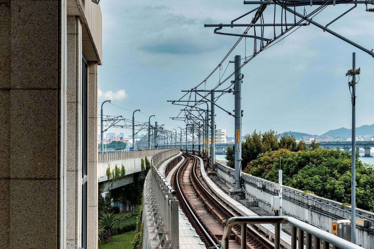 Railway tracks curving near an overhead electrification line with distant green hills.