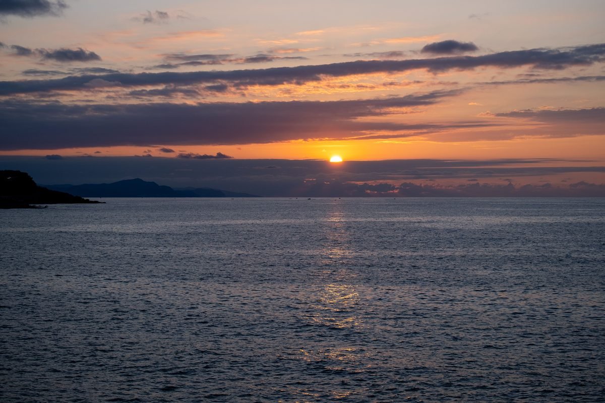 A serene sunset casting warm colors over a calm ocean horizon with distant silhouettes.