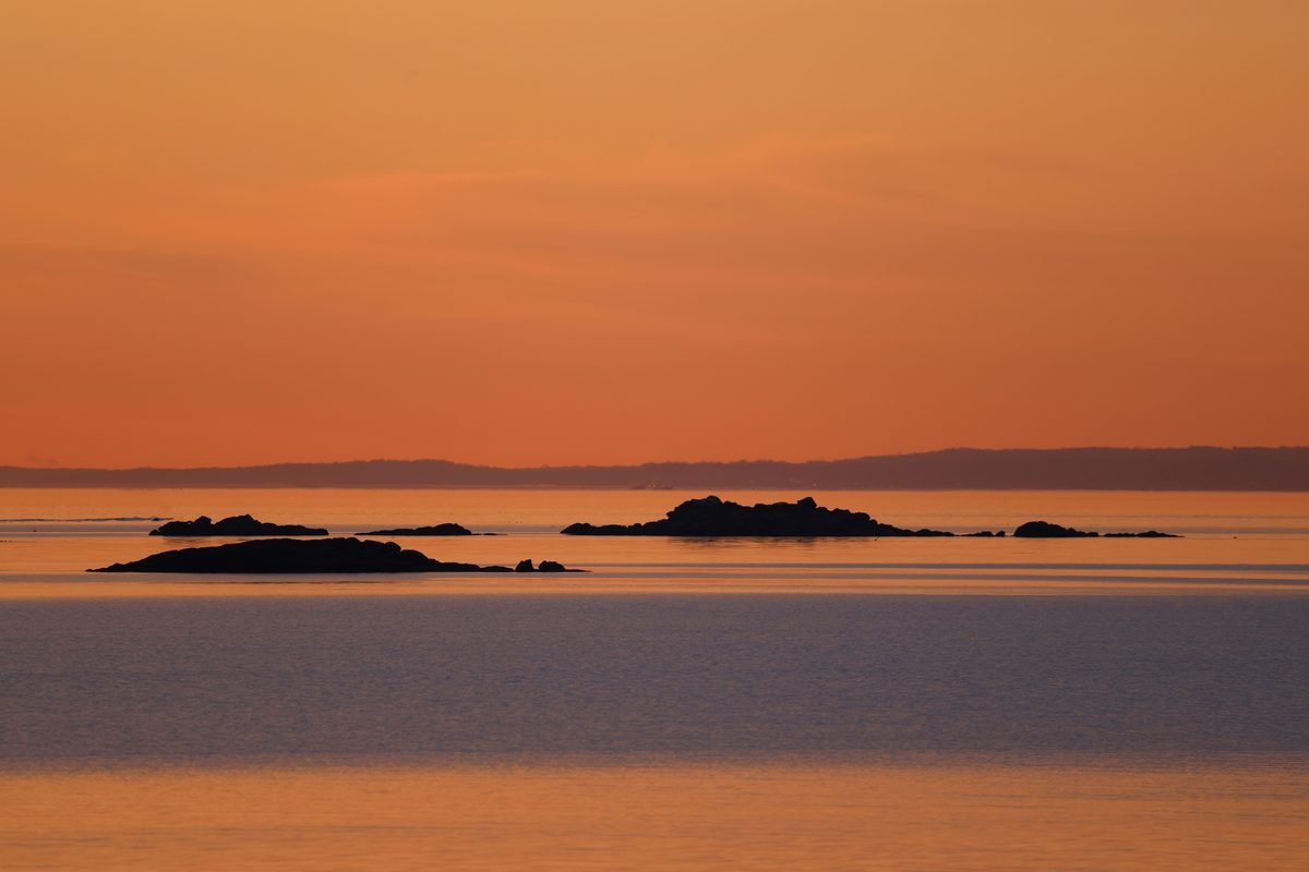 Tranquil view of a sunset over calm coastal waters with distant rock formations.