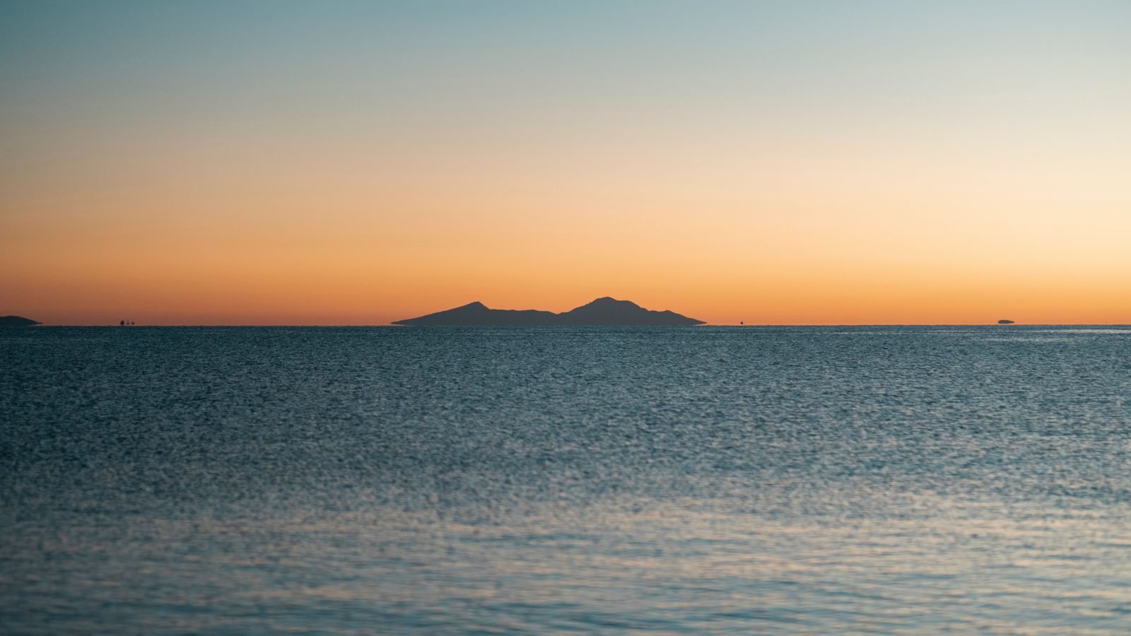 Peaceful view of the ocean during twilight with distant islands under a colorful sky.