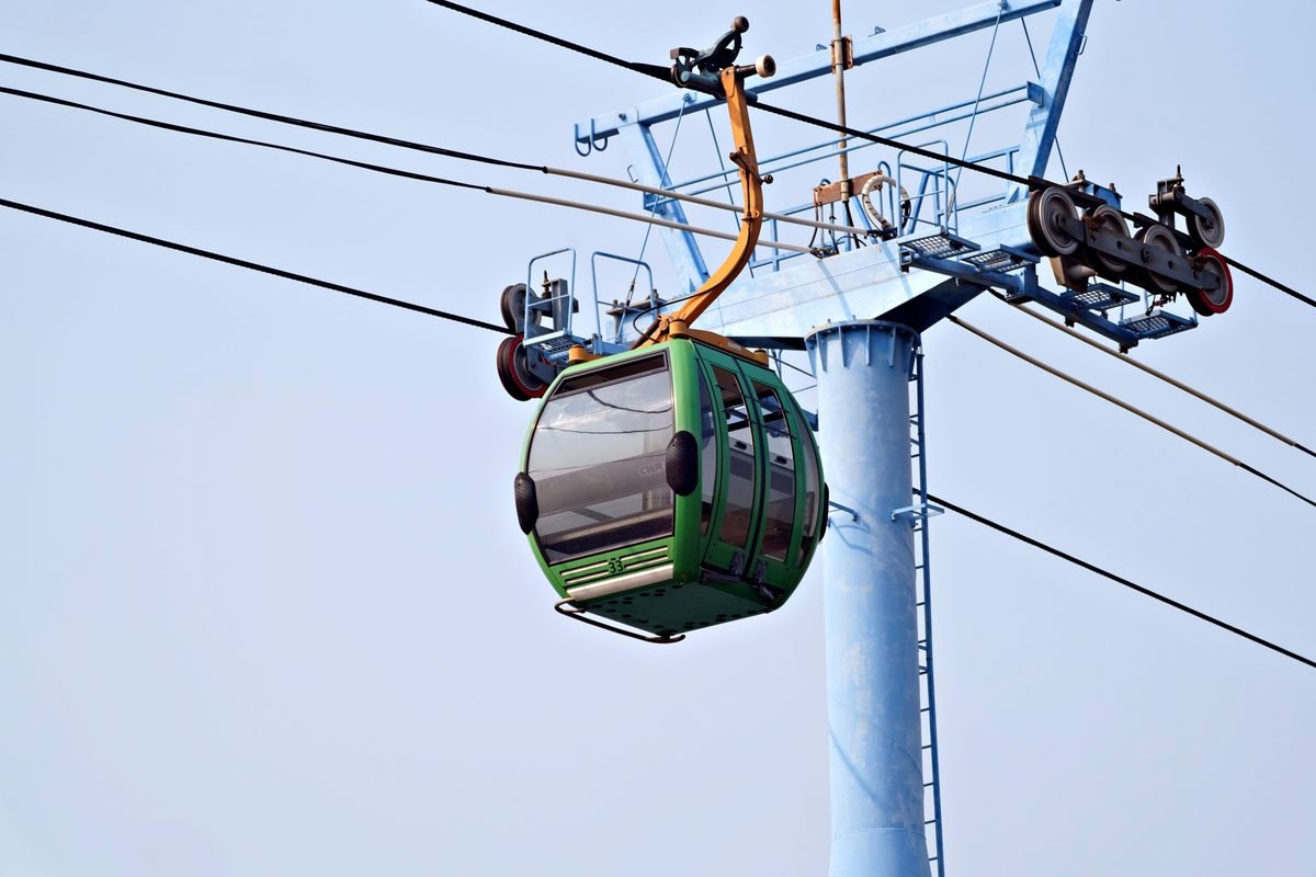 Green cable car cabin on overhead wires against a pale sky