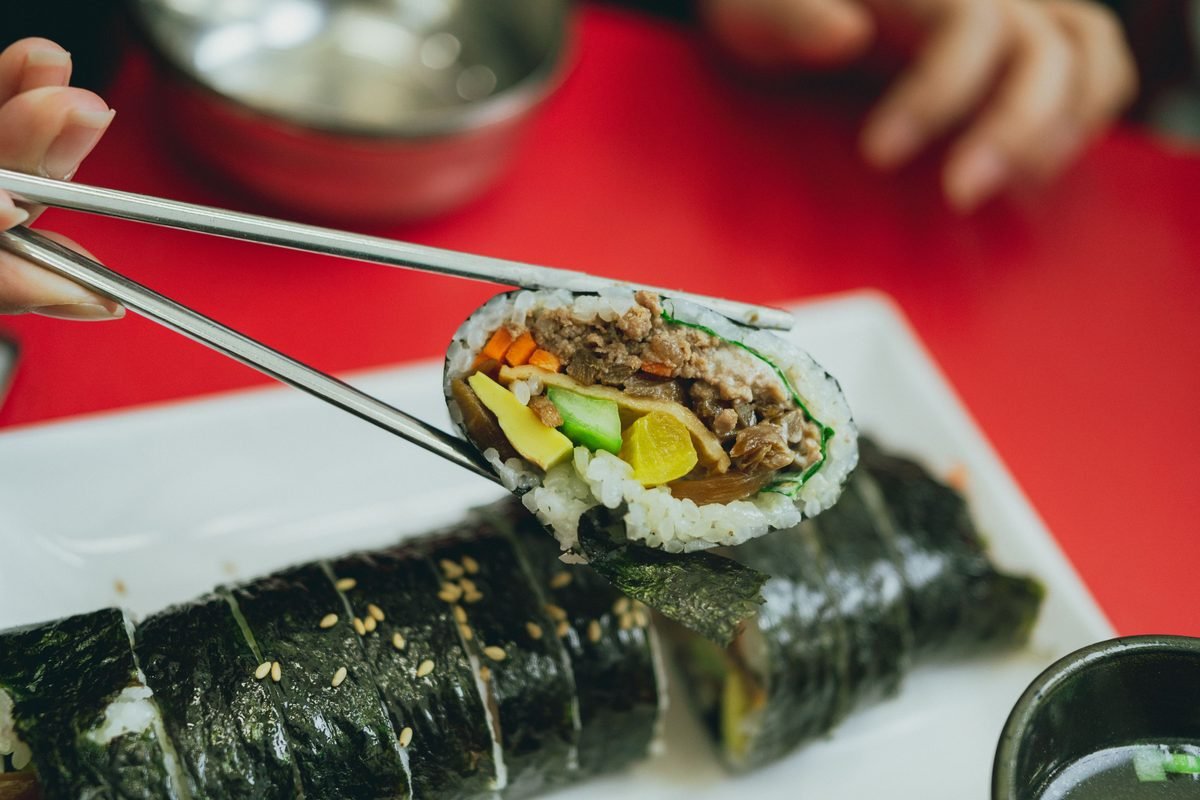 Close-up of sliced Korean gimbap held with chopsticks