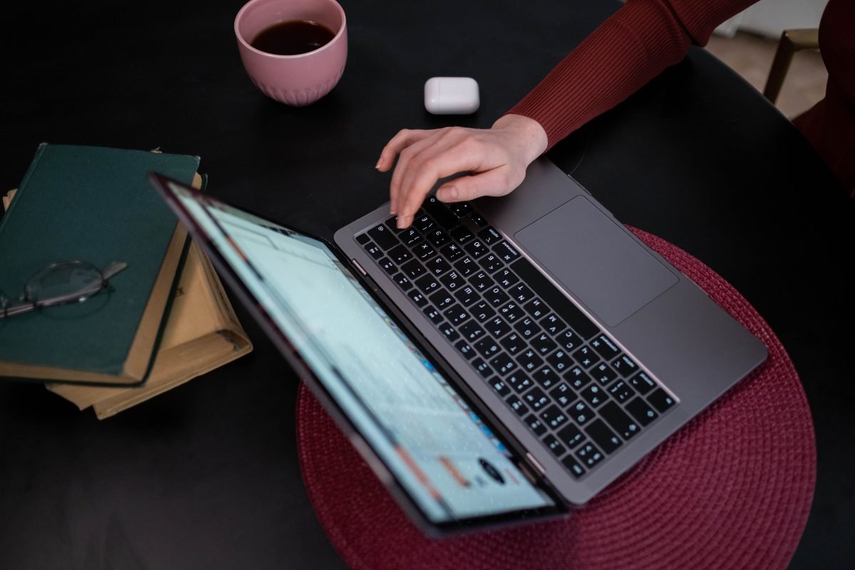 Hands typing on a laptop with a coffee cup and books on a dark table.
